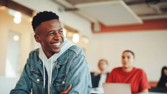 A student smiles from his school desk in casual clothes.