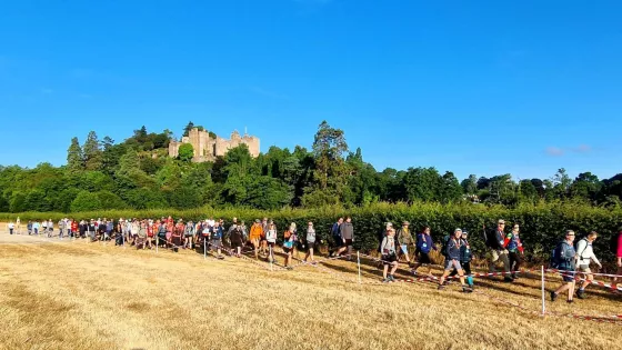Walkers through a field in front of a castle