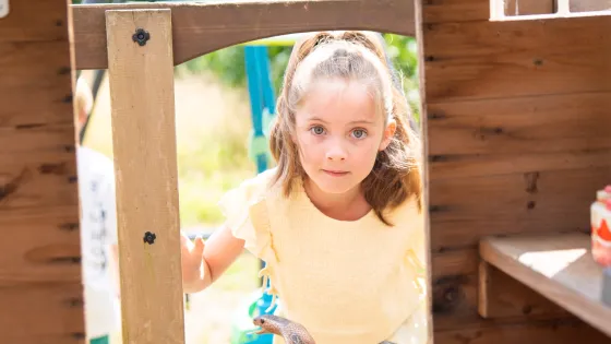 A young girl stands in the door of an outdoor playhouse.
