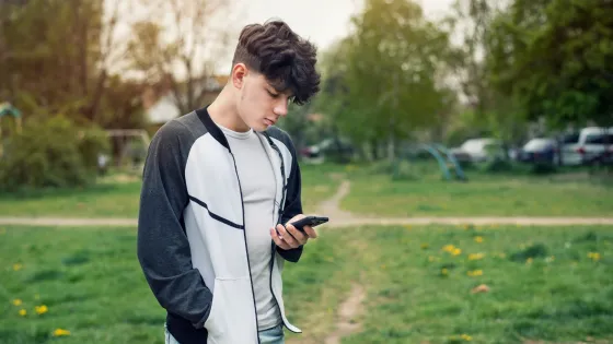 A young man looks solemnly at his phone outside.