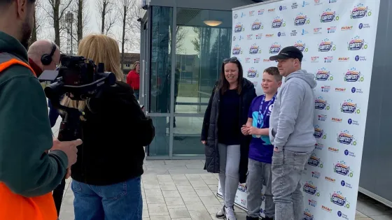 Jamie, a boy with epilepsy, stands with his family in from of a CarFest step and repeat for an interview.