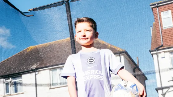 A young boy stands on a trampoline holding a football. 