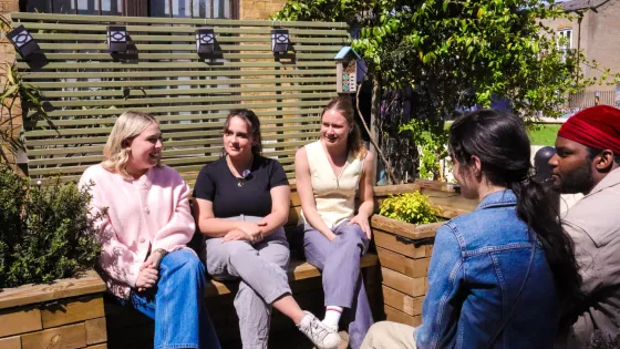 A group of young people chat on outdoor benches.