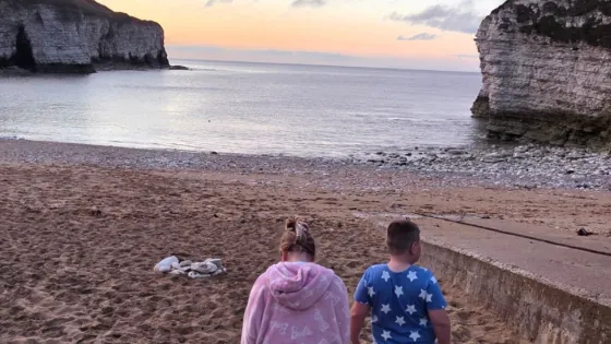 A brother and sister in the pyjamas stand on a beach.