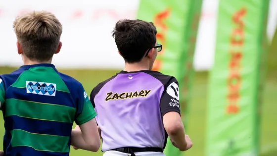 Two boys, one with a t-shirt saying 'Zachary', run through a field.