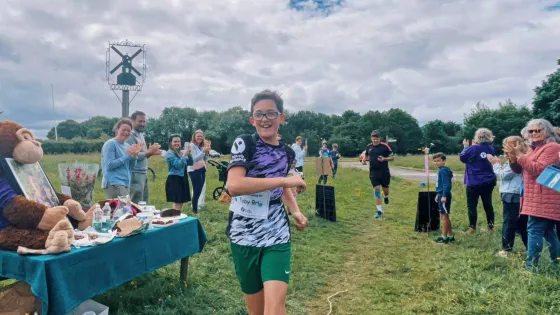 Zac runs past cheering crowds through a grassy field.