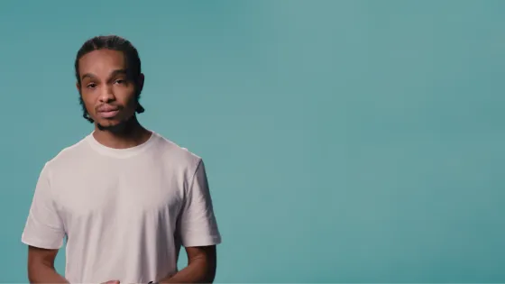 A young man stands looking serious against a teal backdrop.