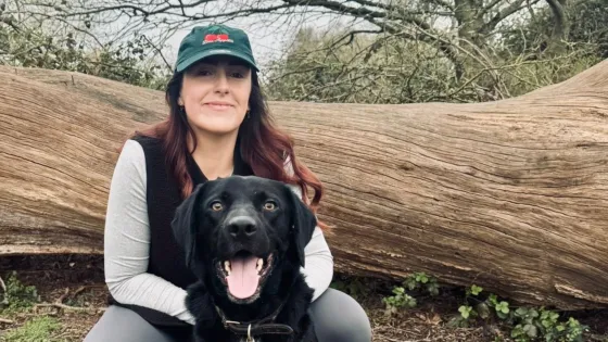 A woman and her dog kneel by a log in a forest.