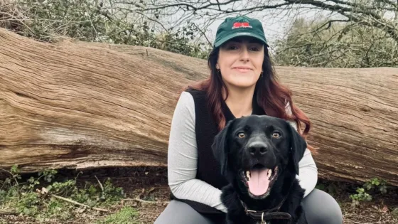 A woman kneels by her dog in a forest.