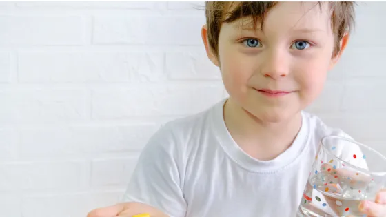 A young boy holds a glass and medication.