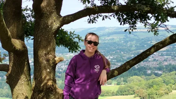 A young woman leans on a tree at a viewing point.
