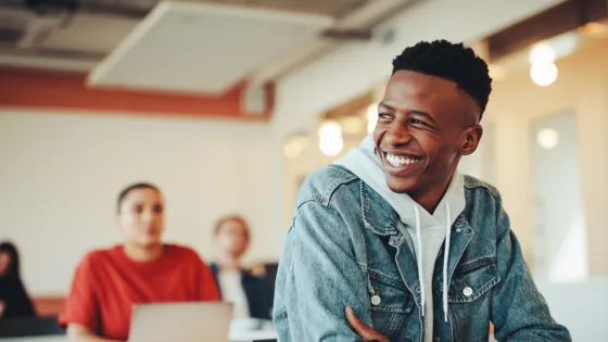A student smiles from his school desk in casual clothes.