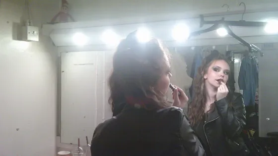 A young woman applies theatrical makeup.