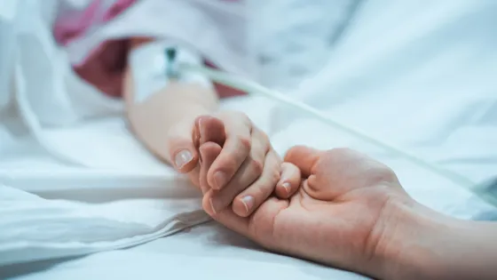 A child in hospital holds a parent's hand.