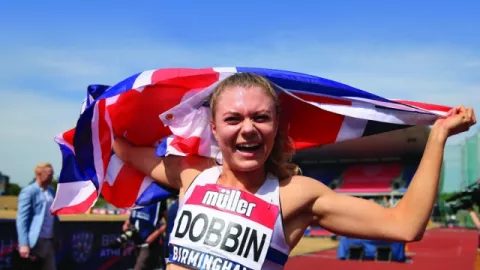 Cheering Olympian Beth Dobbin holds a Union Jack flag up to her head to celebrate a successful race.