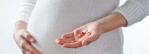 An expecting woman holds a handful of sodium valproate tablets in front of her pregnant belly.