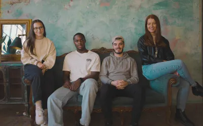 Four young people, two women and two men, sit on a sofa smiling at the camera