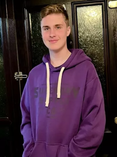 Photograph of teenage boy, wearing a purple hoodie, smiling at the camera