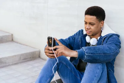 A young person concentrating on his mobile phone with headphones around his neck.