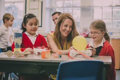 A teacher laughs alongside her students in a classroom.