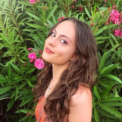 Olivia, a young woman, smiles in a selfie before a flowery bush.