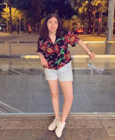A young woman in a floral shirt smiles for a photo taken at night.