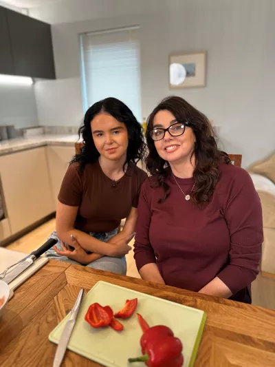 A mother and daughter sit at a kitchen table before a chopping board.