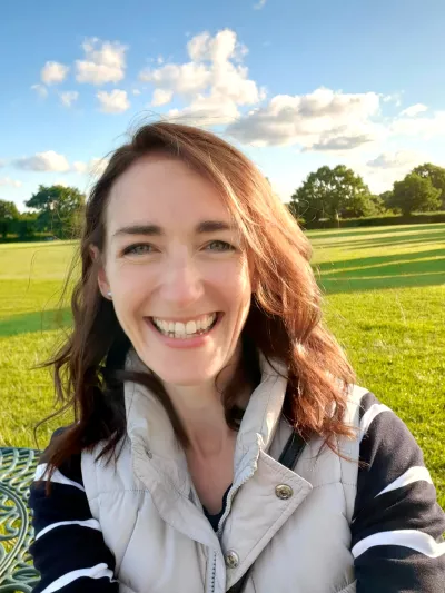 A young woman smiles in a selfie in front of a sunlit field.