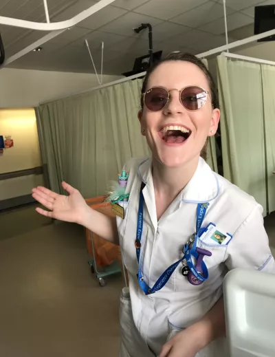 A nurse wearing sunglasses smiles widely to the camera while working on a ward.