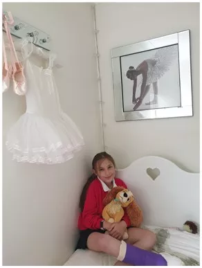 A girl in a leg cast holds a stuffed animal in bed.