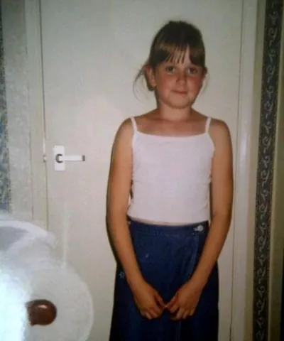 A young girl in a white vest smiles slightly in a posed childhood photograph.