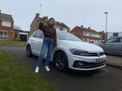 Young woman stands by a car and holds up her car keys.