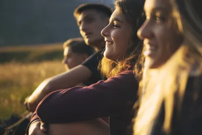 A group of teenagers sit smiling in a row outside in the low light of sunset.
