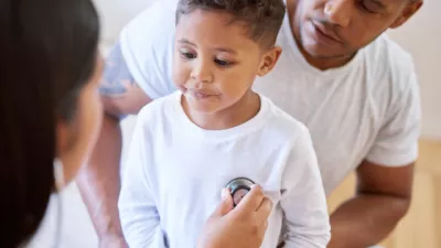 A young boy is being checked over by a healthcare professional while a parent watches over.