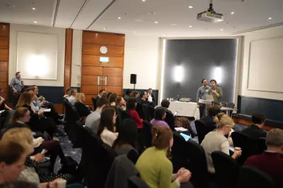 A researcher lectures a large, seated group of people at a research retreat with Young Epilepsy.
