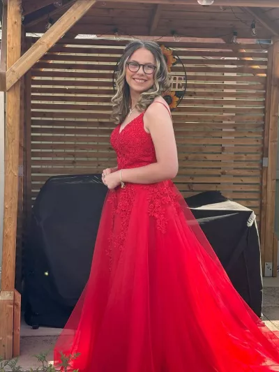Jess, a young woman in glasses, poses gracefully in a long red formal dress.