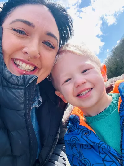 A mother and son smile widely while wearing winter jackets outdoors.