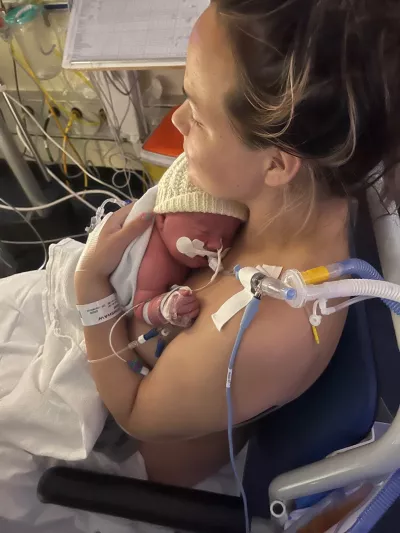 A mother holds her newborn baby in hospital, both connected to many wires.