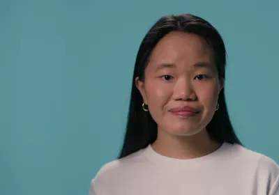 A young Asian girl stands against a blue backdrop wearing a white t-shirt