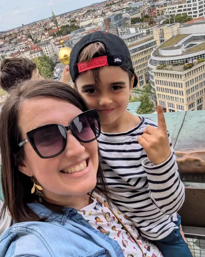 A mother and son take a selfie from a balcony overlooking the high rises of a city.