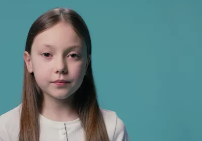 A young Caucasian girl stands against a blue backdrop wearing a white t-shirt