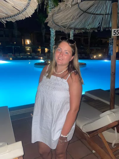 A young woman in a summer dress smiles beside a resort's pool at night.