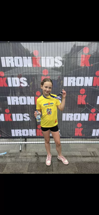 A young girl holds up a sporting medal in front of a step-and-repeat.