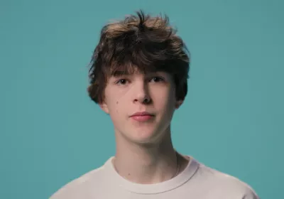 A young boy stands against a blue backdrop wearing a white t-shirt