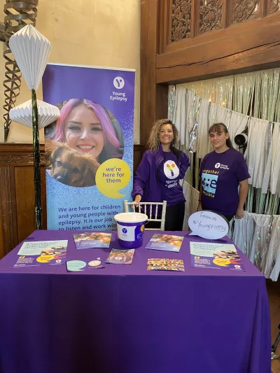 Two Young Epilepsy representatives smile by a fundraising table at a TOWIE event.