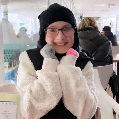 A young woman in a beanie and glasses smiles widely.