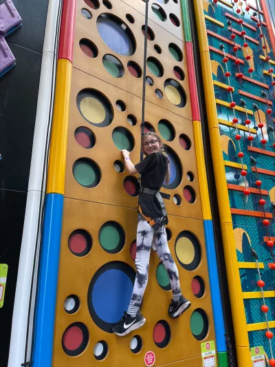 A young woman scales a colourful climbing wall.