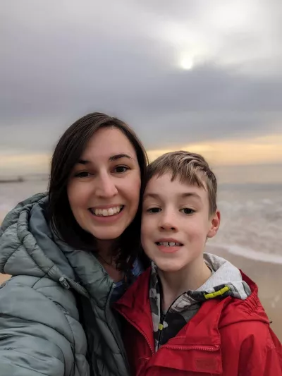 A mother and son smile in a selfie on a beach.