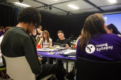 A group of young people make make collages at a table in Young Epilepsy clothing.
