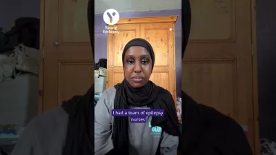 A young woman in a headscarf looks to camera from her home.
